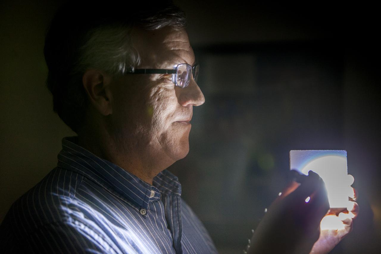 Robert Youngquist, Ph.D., tests a sample disk with a "Solar White" cryogenic selective surface coating with a flash light, demonstrating the coating’s reflective properties. The innovative coating is predicted to reflect more than 99.9 percent of the simulated solar infrared radiation. This technology could enable storing super-cold, or cryogenic, liquids and support systems that shield astronauts against radiation during the Journey to Mars.