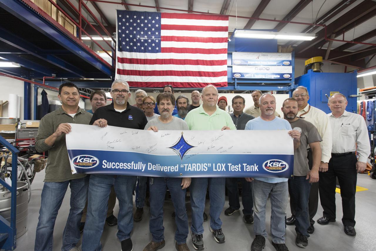 Inside the Prototype Development Laboratory at NASA's Kennedy Space Center in Florida, workers in the lab hold a banner marking the successful delivery of a liquid oxygen test tank called Tardis. Engineers and technicians worked together to develop the tank to build it at the lab to support cryogenic testing at Johnson Space Center's White Sands Test Facility in Las Cruces, New Mexico. The 12-foot-tall, 3,810-pound aluminum tank will be shipped to White Sands for testing. 