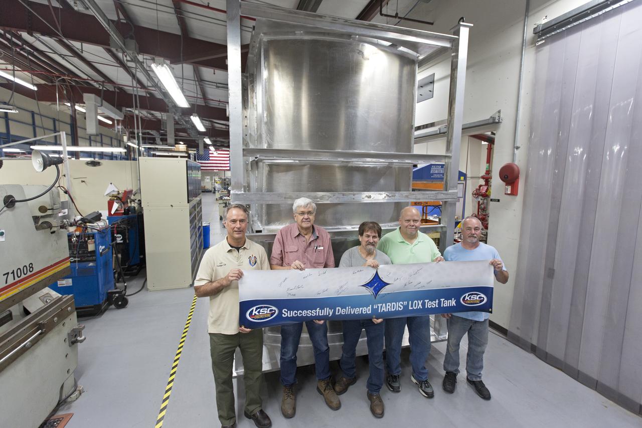 Inside the Prototype Development Laboratory at NASA's Kennedy Space Center in Florida, engineers and technicians hold a banner marking the successful delivery of a liquid oxygen test tank called Tardis. From left, are Todd Steinrock, chief, Fabrication and Development Branch, Prototype Development Lab; David McLaughlin, electrical engineering technician; Phil Stroda, mechanical engineering technician; Perry Dickey, lead electrical engineering technician; and Harold McAmis, lead mechanical engineering technician. Engineers and technicians worked together to develop the tank and build it at the lab to support cryogenic testing at Johnson Space Center's White Sands Test Facility in Las Cruces, New Mexico. The 12-foot-tall, 3,810-pound aluminum tank will be shipped to White Sands for testing. 