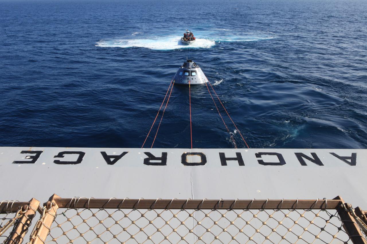 Off the rear of the USS Anchorage, the Orion test article is pulled in by a winch line at the rear of the USS Anchorage’s well deck that brings the capsule into the ship, along with four manned LLAMAs (Line Load Attenuation Mechanism Assembly) that control the capsule’s side-to-side movement and a tending line attached to a rigid hull inflatable boat for controlling Orion’s movement behind the ship. The Underway Recovery Test 6 (URT-6) is spearheaded by Kennedy Space Center's NASA Recovery Team. In partnership with the U.S. Navy, the testing will provide important data that is being used to improve recovery procedures and hardware ahead of Orion's next flight, Exploration Mission-1, when it splashes down in the Pacific Ocean.