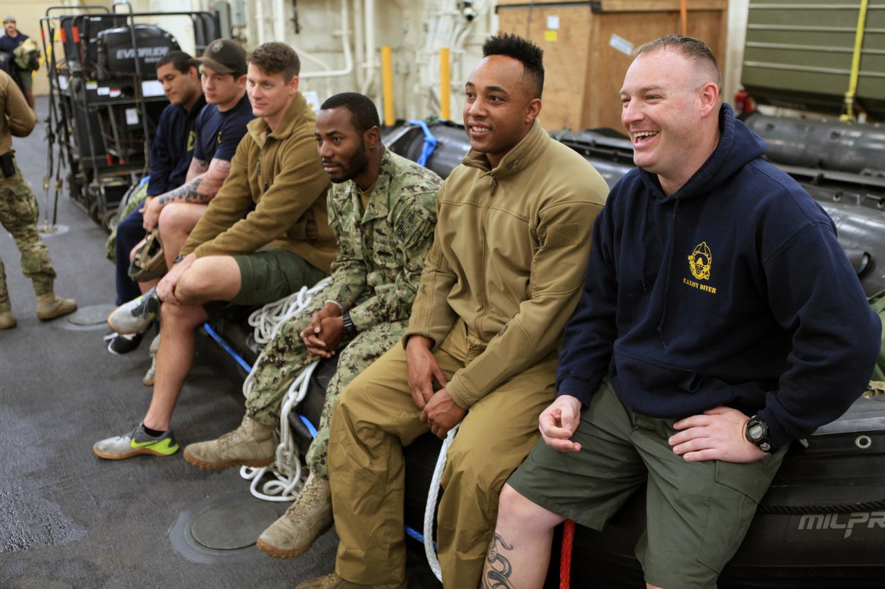 Navy diver Michael Tuft (far right) and his team wait to be called for their part in Underway Recovery Test 6 aboard the USS Anchorage. The divers will be the first people astronauts aboard the Orion spacecraft see when they splash down in the Pacific Ocean after Exploration Mission-2. The testing with the NASA Recovery Team and the U.S. Navy will provide important data that is being used to improve recovery procedures and hardware ahead of Orion's next flight, Exploration Mission-1, when it splashes down in the Pacific Ocean.
