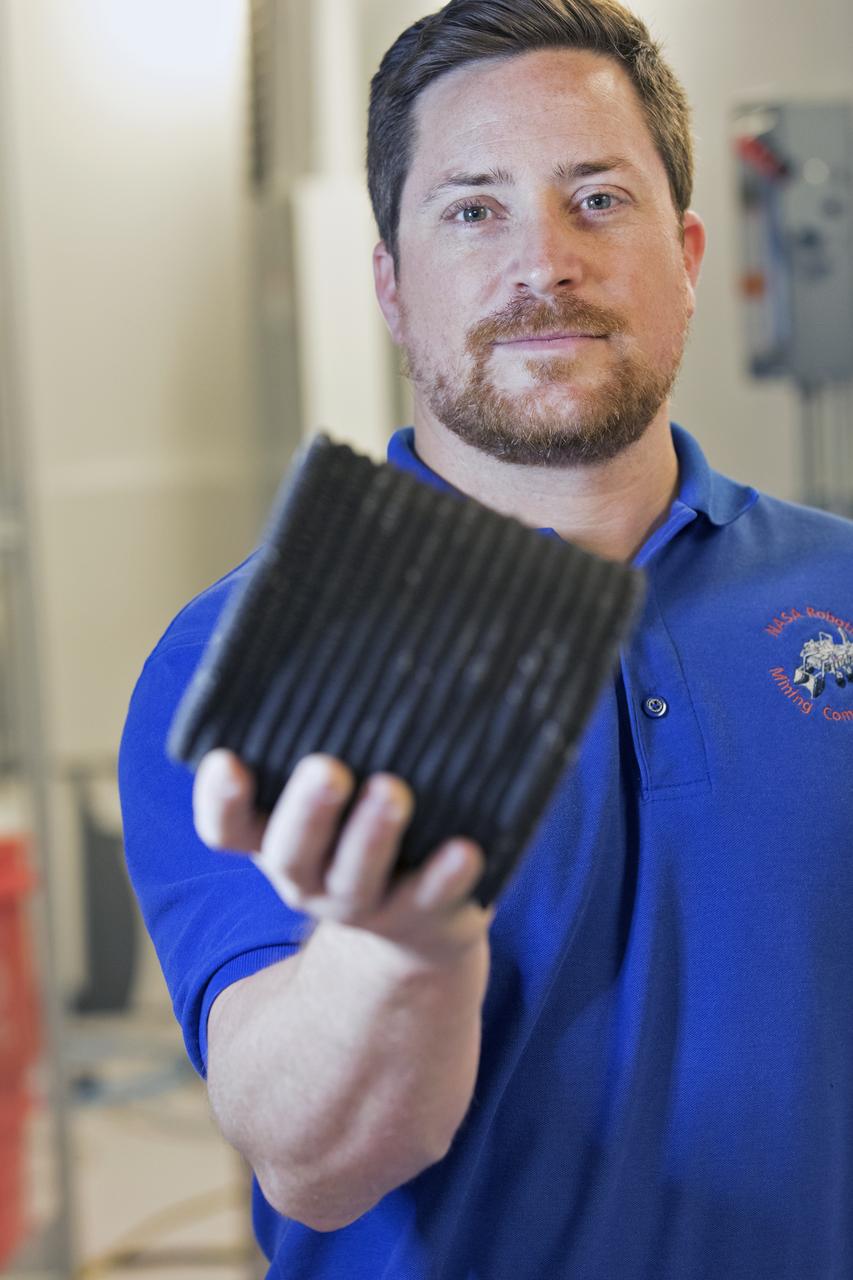 Nathan Gelino, a NASA research engineer at Kennedy Space Center in Florida displays a 3-D printed cylinder used for compression testing. Engineers at the center’s Swamp Works measured how much force it takes to break the structure before moving on to 3-D printing with a simulated lunar regolith, or dirt, and polymers. Next, Gelino and his group are working on a Zero Launch Mass 3-D printer that can be used for construction projects on the Moon and Mars, even for troops in remote locations here on Earth. Zero launch mass refers to the fact that the printer uses these pellets to prove that space explorers can use resources at their destination instead of taking everything with them, saving them launch mass and money.  Gelino and his team are working with Marshall Space Flight Center in Huntsville, Alabama, and the U.S. Army Corps of Engineers to develop a system that can 3-D print barracks in remote locations on Earth, using the resources they have where they are. 