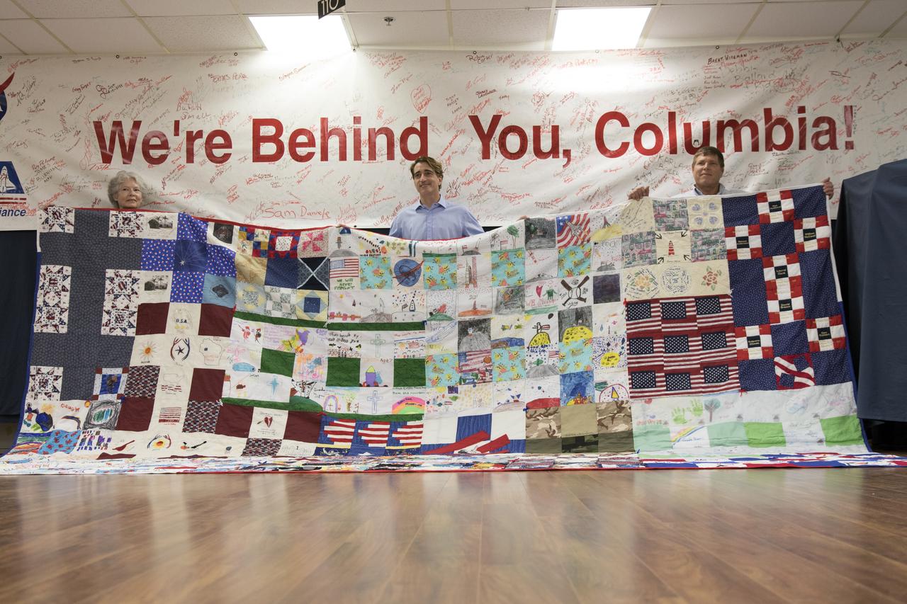 A giant hand-made quilt in honor of space shuttle Columbia and her crew was turned over to the Columbia Preservation Room inside the Vehicle Assembly Building at NASA's Kennedy Space Center in Florida. The quilt was made by Katherine Walsh, a lifelong NASA and space program fan originally from Kentucky. From left, behind the quilt are Janet Phillips, property custodian in Kennedy's Office of Procurement; Mike Ciannilli, Apollo, Challenger, Columbia Lessons Learned Program manager; and Kevin Panik, customer advocate in Spaceport Integration.