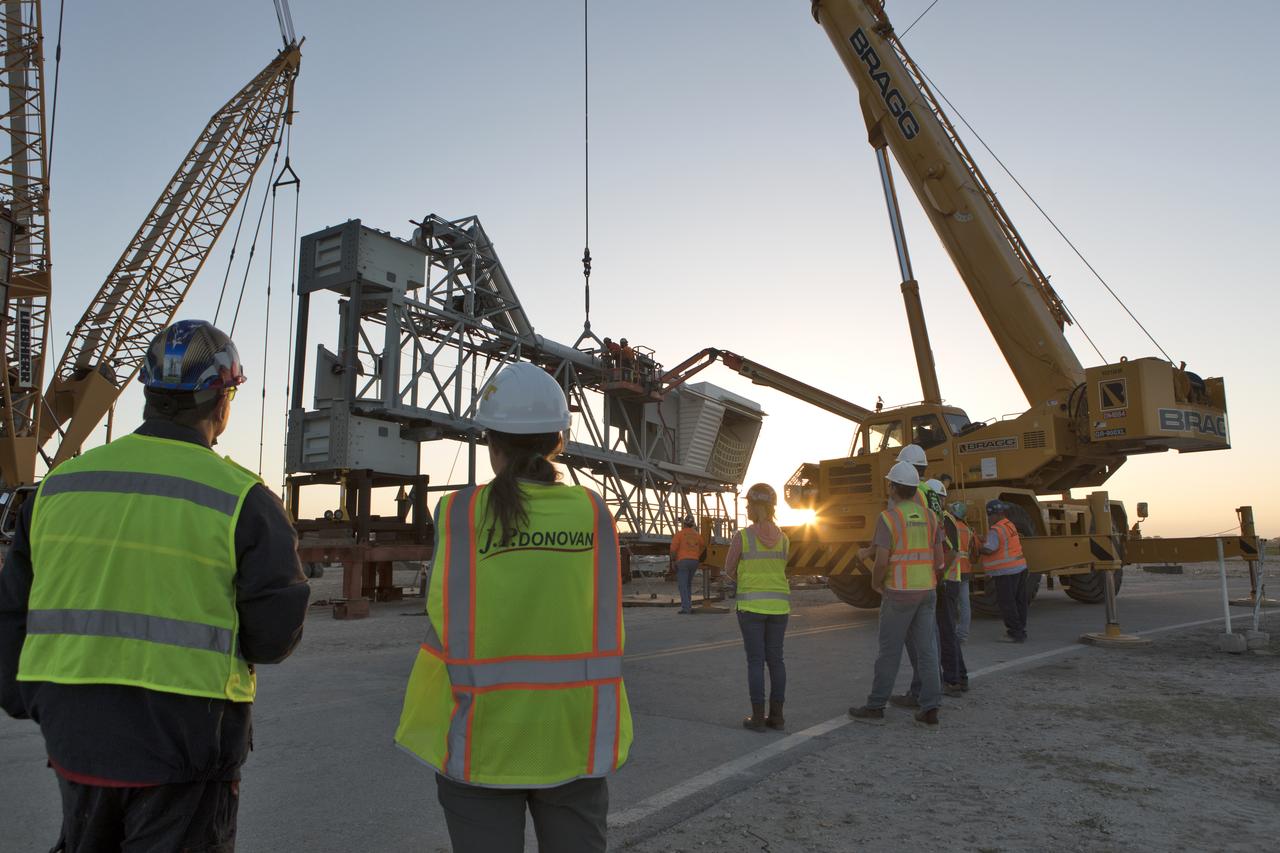 Under the watchful eye of technicians and engineers, a crane is prepared to lift the Orion crew access arm (CAA) so it can be attached to the mobile launcher (ML) at NASA's Kennedy Space Center in Florida. The arm will be installed at about the 274-foot level on the ML tower. NASA's Exploration Ground Systems organization has been overseeing installation of umbilicals and other launch accessories on the 380-foot-tall ML in preparation for stacking the first launch of the Space launch System, or SLS, rocket with an Orion spacecraft. The CAA is designed to rotate from its retracted position and line up with Orion's crew hatch providing entry for astronauts and technicians.