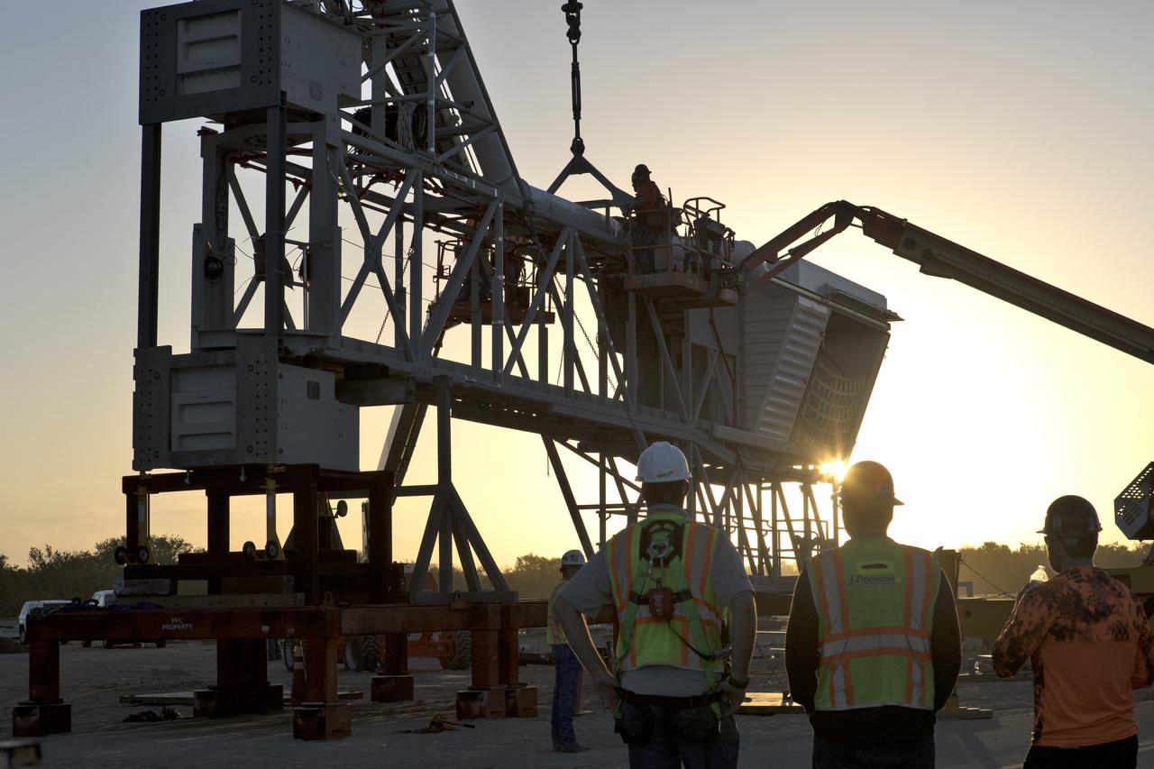 Under the watchful eye of technicians and engineers, a crane is prepared to lift the Orion crew access arm (CAA) so it can be attached to the mobile launcher (ML) at NASA's Kennedy Space Center in Florida. The arm will be installed at about the 274-foot level on the ML tower. NASA's Exploration Ground Systems organization has been overseeing installation of umbilicals and other launch accessories on the 380-foot-tall ML in preparation for stacking the first launch of the Space launch System, or SLS, rocket with an Orion spacecraft. The CAA is designed to rotate from its retracted position and line up with Orion's crew hatch providing entry for astronauts and technicians.