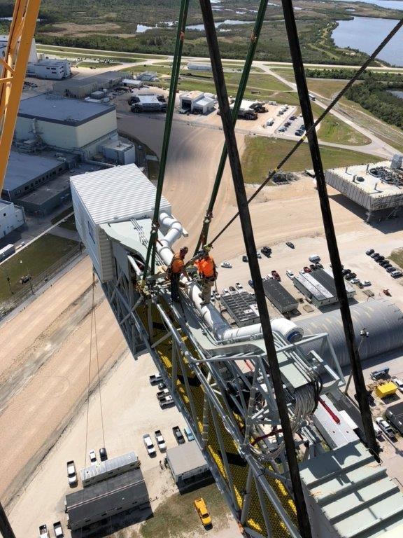 Viewed from the 274-foot level mobile launcher (ML), technicians help install the Orion crew access arm (CAA) to the tower at NASA's Kennedy Space Center in Florida. NASA's Exploration Ground Systems organization has been overseeing installation of umbilicals and other launch accessories on the 380-foot-tall ML in preparation for stacking the first launch of the Space launch System (SLS), rocket with an Orion spacecraft. The CAA is designed to rotate from its retracted position and line up with Orion's crew hatch providing entry for astronauts and technicians.
