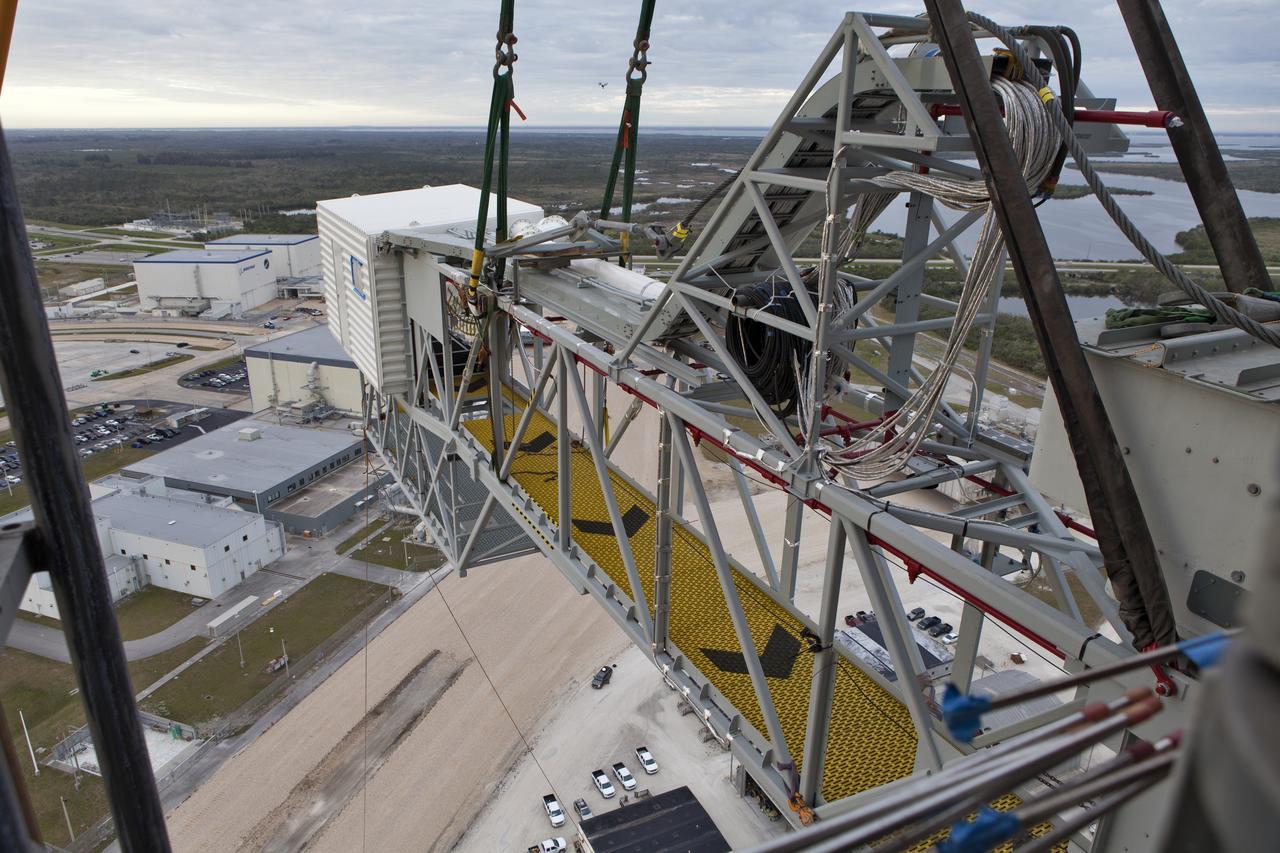Viewed from the 274-foot level mobile launcher (ML), a crane positions the Orion crew access arm (CAA) so it can be attached to the tower that will support the Space launch System (SLS) rocket at NASA's Kennedy Space Center in Florida. NASA's Exploration Ground Systems organization has been overseeing installation of umbilicals and other launch accessories on the 380-foot-tall ML in preparation for stacking the first launch of the SLS, rocket with an Orion spacecraft. The CAA is designed to rotate from its retracted position and line up with Orion's crew hatch providing entry for astronauts and technicians.