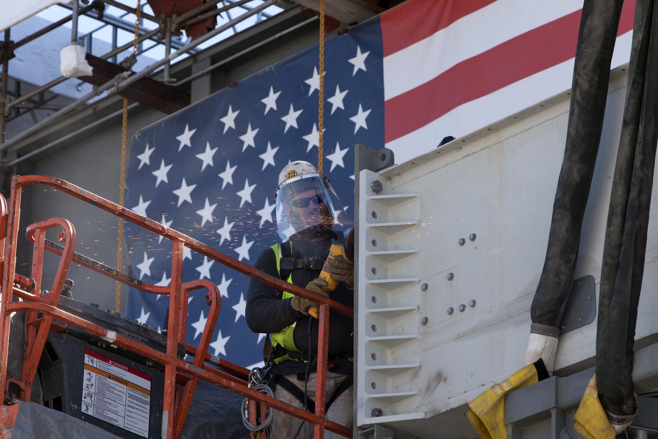 A construction worker with JP Donovan helps prepare the Interim Cryogenic Propulsion Stage Umbilical (ICPSU) for installation high up on the tower of the mobile launcher (ML) at NASA's Kennedy Space Center in Florida. The last of the large umbilicals to be installed, the ICPSU will provide super-cooled hydrogen and liquid oxygen to the Space Launch System (SLS) rocket's interim cryogenic propulsion stage, or upper stage, at T-0 for Exploration Mission-1. The umbilical will be located at about the 240-foot-level of the mobile launcher and will supply fuel, oxidizer, gaseous helium, hazardous gas leak detection, electrical commodities and environment control systems to the upper stage of the SLS rocket during launch. Exploration Ground Systems is overseeing installation of the umbilicals on the ML. 