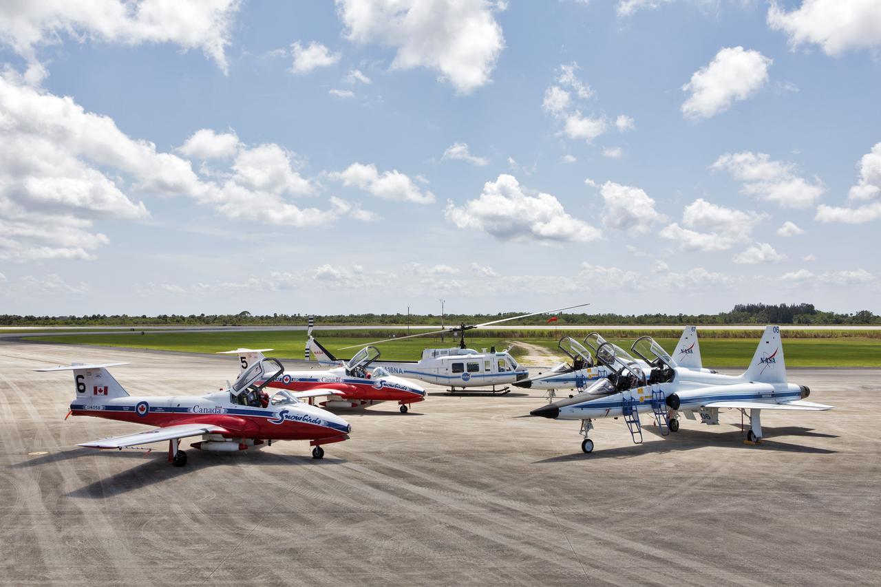 Several types of aircraft are on the tarmac at the Shuttle Landing Facility (SLF) at NASA's Kennedy Space in Florida. From left, are two Canadian Forces Snowbird CF-18 jets, a NASA Huey helicopter, and two NASA T-38 trainer aircraft. The Canadian Forces Snowbirds performed aerial maneuvers over Kennedy and Cape Canaveral Air Force Station during a practice flight on May 9, 2018, between their scheduled air shows.