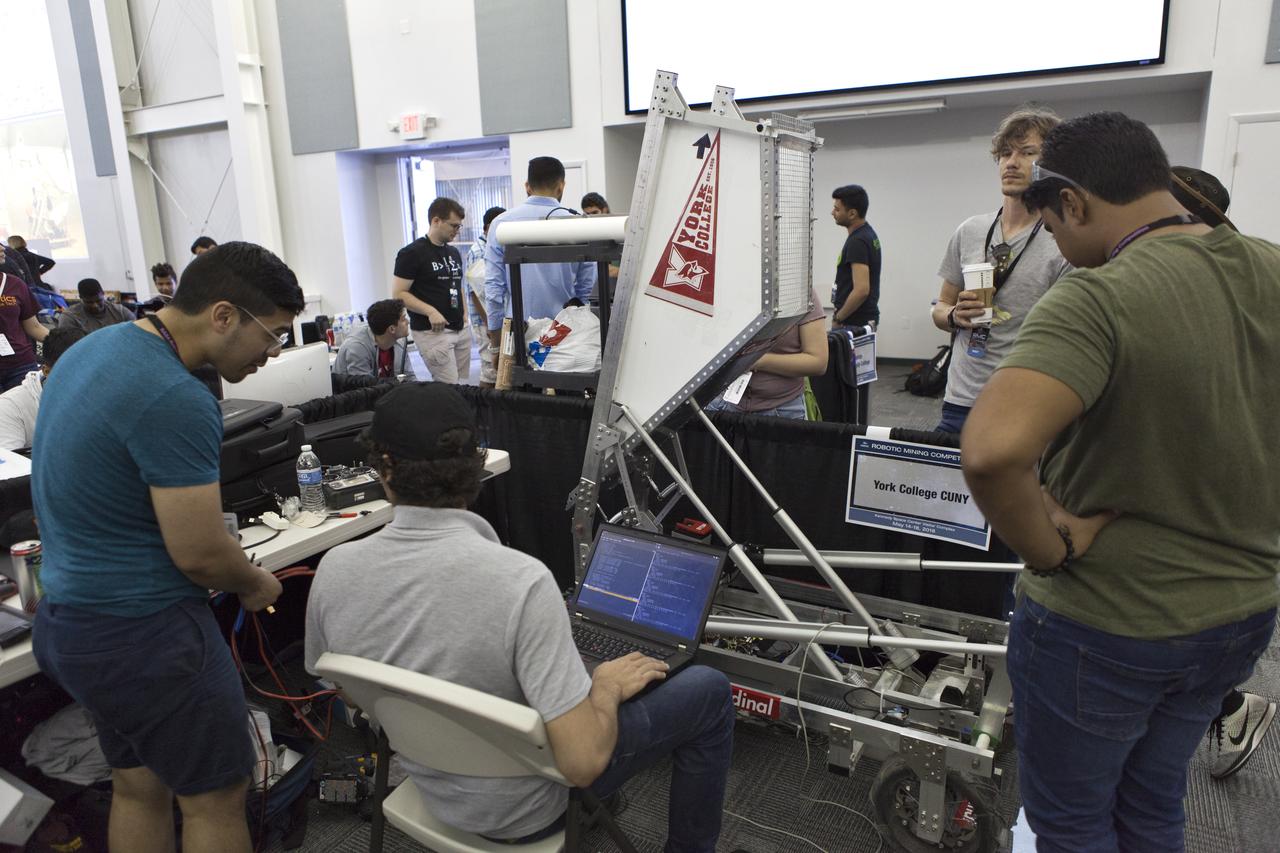 Team members from York College CUNY make adjustments to their robot miner for its turn in the mining arena on the fourth day of NASA's 9th Robotic Mining Competition, May 17, inside the RobotPits at NASA's Kennedy Space Center Visitor Complex in Florida. More than 40 student teams from colleges and universities around the U.S. are using their mining robots to dig in a supersized sandbox filled with BP-1, or simulated Lunar soil, gravel and rocks, and participate in other competition requirements. The Robotic Mining Competition is a NASA Human Exploration and Operations Mission Directorate project designed to encourage students in science, technology, engineering and math, or STEM fields. The project provides a competitive environment to foster innovative ideas and solutions that could be used on NASA's deep space missions.