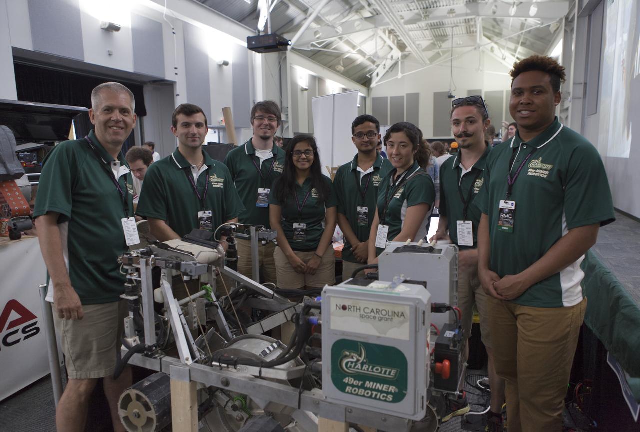 Team members and their faculty advisor, far left, from The University of North Carolina at Charlotte pause with their robot miner in the RobotPits on the fourth day of NASA's 9th Robotic Mining Competition, May 17, at NASA's Kennedy Space Center Visitor Complex in Florida. More than 40 student teams from colleges and universities around the U.S. will use their mining robots to dig in a supersized sandbox filled with BP-1, or simulated Lunar soil, gravel and rocks, and participate in other competition requirements. The Robotic Mining Competition is a NASA Human Exploration and Operations Mission Directorate project designed to encourage students in science, technology, engineering and math, or STEM fields. The project provides a competitive environment to foster innovative ideas and solutions that could be used on NASA's deep space missions.
