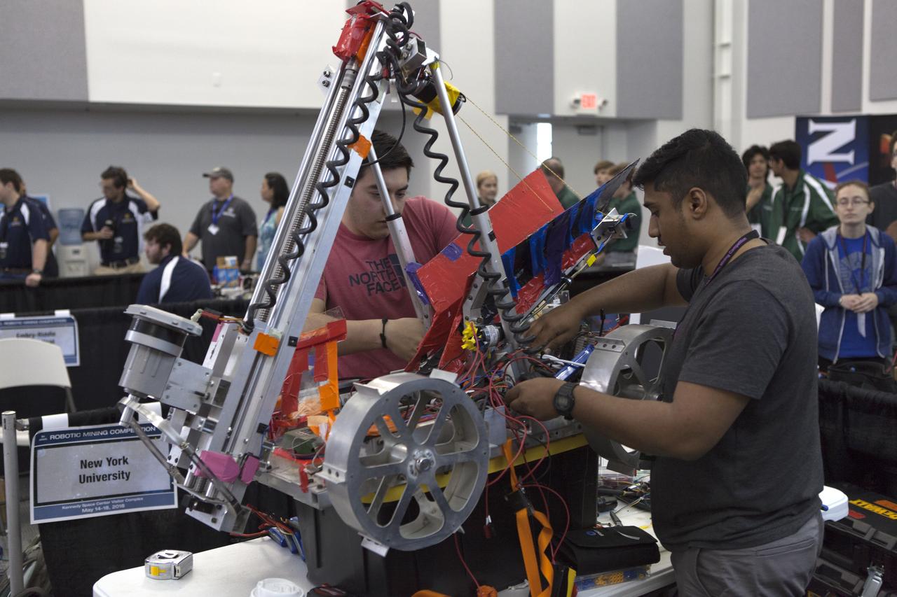 Team members from New York University work on their robot miner in the RobotPits on the fourth day of NASA's 9th Robotic Mining Competition, May 17, at NASA's Kennedy Space Center Visitor Complex in Florida. More than 40 student teams from colleges and universities around the U.S. are using their mining robots to dig in a supersized sandbox filled with BP-1, or simulated Lunar soil, gravel and rocks, and participate in other competition requirements. The Robotic Mining Competition is a NASA Human Exploration and Operations Mission Directorate project designed to encourage students in science, technology, engineering and math, or STEM fields. The project provides a competitive environment to foster innovative ideas and solutions that could be used on NASA's deep space missions.