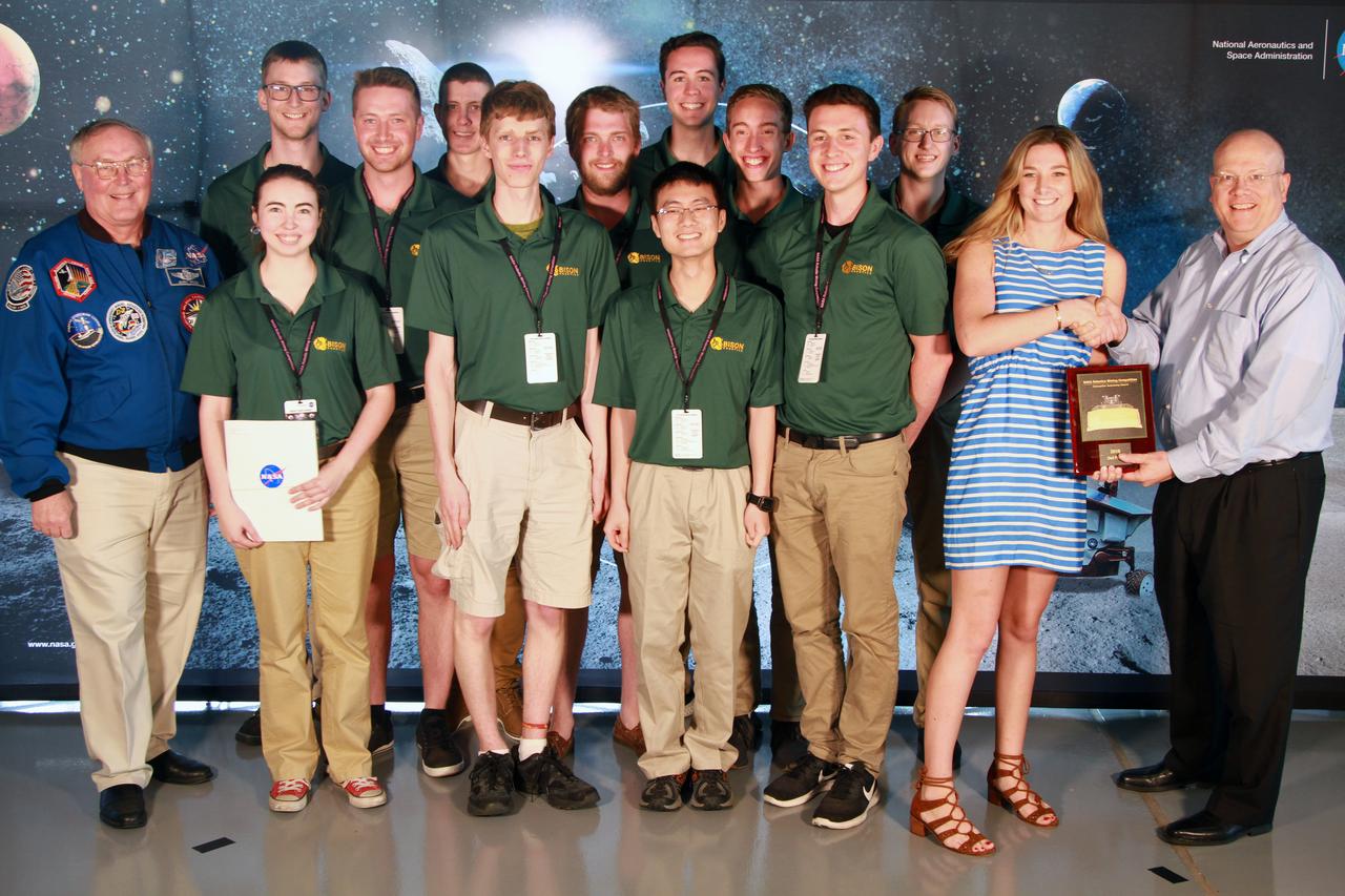NASA's 9th Annual Robotic Mining Competition concludes with an awards ceremony May 18, 2018, at the Apollo/Saturn V Center at the Kennedy Space Center Visitor Complex in Florida. The team from North Dakota State University in collaboration with James Madison University received second place in the Caterpillar Award for Autonomy. At left is retired NASA astronaut Jerry Ross. At right is Eric Reiners, program manager with the Innovation & Technology Development Division of Caterpillar Inc. More than 40 student teams from colleges and universities around the U.S. participated in the competition, May 14-18, by using their mining robots to dig in a supersized sandbox filled with BP-1, or simulated lunar soil, gravel and rocks, and participate in other competition requirements. The Robotic Mining Competition is a NASA Human Exploration and Operations Mission Directorate project designed to encourage students in science, technology, engineering and math, or STEM fields. The project provides a competitive environment to foster innovative ideas and solutions that could be used on NASA's deep space missions. 