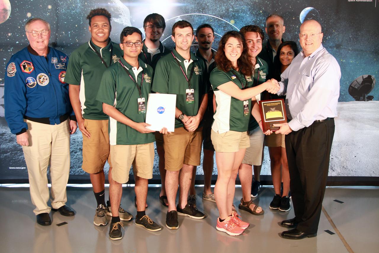 NASA's 9th Annual Robotic Mining Competition concludes with an awards ceremony May 18, 2018, at the Apollo/Saturn V Center at the Kennedy Space Center Visitor Complex in Florida. The team from the University of North Carolina at Charlotte received third place in the Caterpillar Award for Autonomy. At left is retired NASA astronaut Jerry Ross. At right is Eric Reiners, program manager with the Innovation & Technology Development Division of Caterpillar Inc. More than 40 student teams from colleges and universities around the U.S. participated in the competition, May 14-18, by using their mining robots to dig in a supersized sandbox filled with BP-1, or simulated lunar soil, gravel and rocks, and participate in other competition requirements. The Robotic Mining Competition is a NASA Human Exploration and Operations Mission Directorate project designed to encourage students in science, technology, engineering and math, or STEM fields. The project provides a competitive environment to foster innovative ideas and solutions that could be used on NASA's deep space missions.