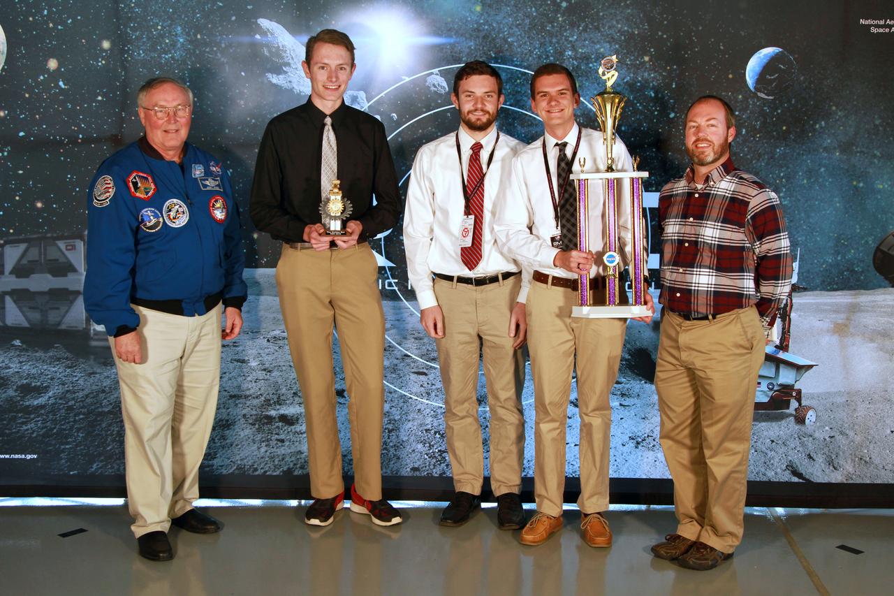 NASA's 9th Annual Robotic Mining Competition concludes with an awards ceremony May 18, 2018, at the Apollo/Saturn V Center at the Kennedy Space Center Visitor Complex in Florida. The University of Alabama Team Astrobotics received the Efficient Use of Communications Power Award. At left is retired NASA astronaut Jerry Ross. At right is Kurt Leucht, a NASA engineer in Swamp Works and event emcee. More than 40 student teams from colleges and universities around the U.S. participated in the competition, May 14-18, by using their mining robots to dig in a supersized sandbox filled with BP-1, or simulated lunar soil, gravel and rocks, and participate in other competition requirements. The Robotic Mining Competition is a NASA Human Exploration and Operations Mission Directorate project designed to encourage students in science, technology, engineering and math, or STEM fields. The project provides a competitive environment to foster innovative ideas and solutions that could be used on NASA's deep space missions.