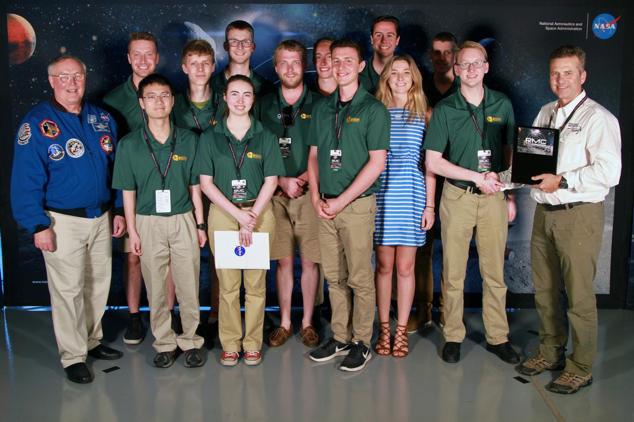 NASA's 9th Annual Robotic Mining Competition concludes with an awards ceremony May 18, 2018, at the Apollo/Saturn V Center at the Kennedy Space Center Visitor Complex in Florida. The team from North Dakota University in collaboration with James Madison University received second place in the On-Site Mining Award. At left is retired NASA astronaut Jerry Ross. At right is Rob Mueller, lead mining judge. More than 40 student teams from colleges and universities around the U.S. participated in the competition, May 14-18, by using their mining robots to dig in a supersized sandbox filled with BP-1, or simulated lunar soil, gravel and rocks, and participate in other competition requirements. The Robotic Mining Competition is a NASA Human Exploration and Operations Mission Directorate project designed to encourage students in science, technology, engineering and math, or STEM fields. The project provides a competitive environment to foster innovative ideas and solutions that could be used on NASA's deep space missions.