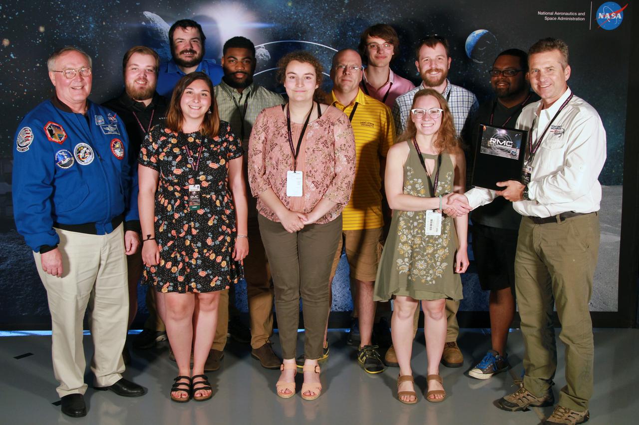 NASA's 9th Annual Robotic Mining Competition concludes with an awards ceremony May 18, 2018, at the Apollo/Saturn V Center at the Kennedy Space Center Visitor Complex in Florida. The team from Kent State University received third place in the On-Site Mining Award. At left is retired NASA astronaut Jerry Ross. At right is Rob Mueller, lead mining judge. More than 40 student teams from colleges and universities around the U.S. participated in the competition, May 14-18, by using their mining robots to dig in a supersized sandbox filled with BP-1, or simulated lunar soil, gravel and rocks, and participate in other competition requirements. The Robotic Mining Competition is a NASA Human Exploration and Operations Mission Directorate project designed to encourage students in science, technology, engineering and math, or STEM fields. The project provides a competitive environment to foster innovative ideas and solutions that could be used on NASA's deep space missions.
