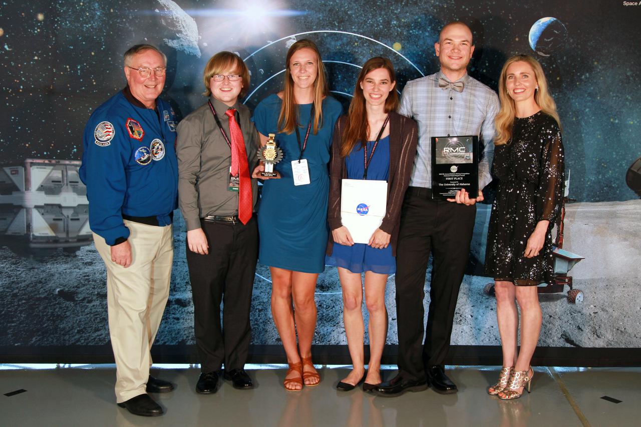 NASA's 9th Annual Robotic Mining Competition concludes with an awards ceremony May 18, 2018, at the Apollo/Saturn V Center at the Kennedy Space Center Visitor Complex in Florida. The University of Alabama Team Astrobotics received first place in the Outreach Project category. At left is retired NASA astronaut Jerry Ross. At right is Bethanne Hull, NASA Education specialist and lead Outreach Project judge. More than 40 student teams from colleges and universities around the U.S. participated in the competition, May 14-18, by using their mining robots to dig in a supersized sandbox filled with BP-1, or simulated lunar soil, gravel and rocks, and participate in other competition requirements. The Robotic Mining Competition is a NASA Human Exploration and Operations Mission Directorate project designed to encourage students in science, technology, engineering and math, or STEM fields. The project provides a competitive environment to foster innovative ideas and solutions that could be used on NASA's deep space missions.