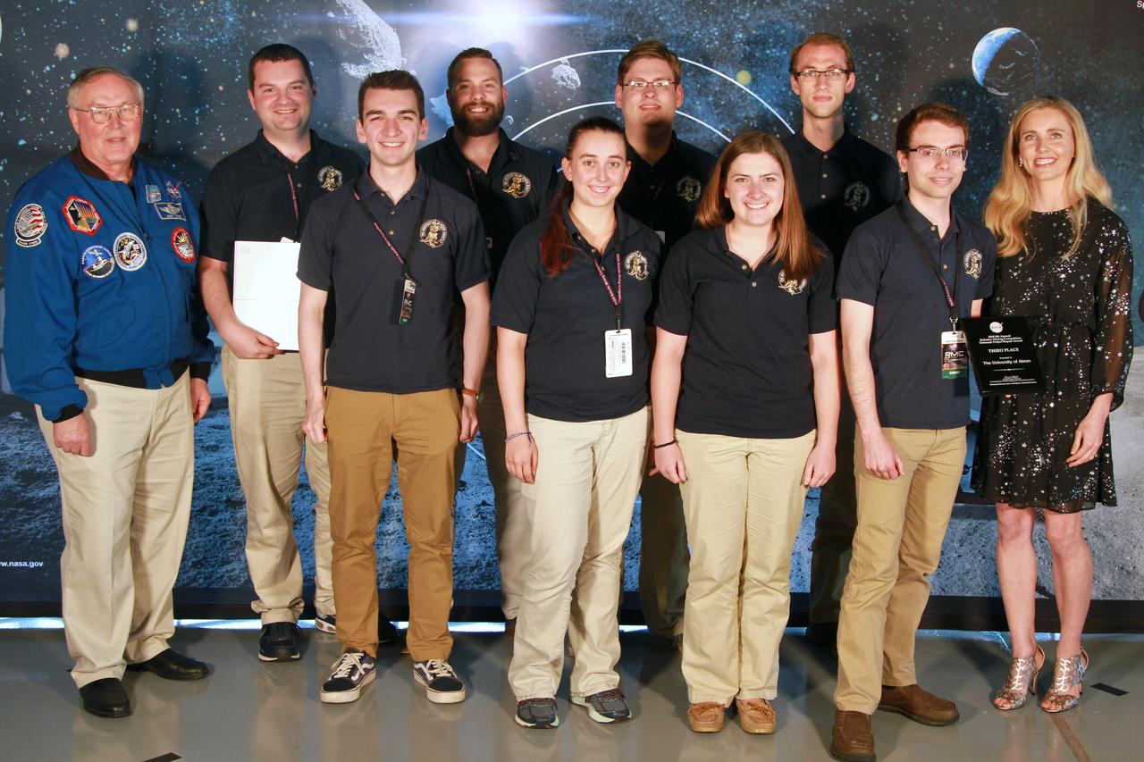 NASA's 9th Annual Robotic Mining Competition concludes with an awards ceremony May 18, 2018, at the Apollo/Saturn V Center at the Kennedy Space Center Visitor Complex in Florida. The team from The University of Akron received third place in the Outreach Project category. At left is retired NASA astronaut Jerry Ross. At right is Bethanne Hull, NASA Education specialist and lead Outreach Project judge. More than 40 student teams from colleges and universities around the U.S. participated in the competition, May 14-18, by using their mining robots to dig in a supersized sandbox filled with BP-1, or simulated lunar soil, gravel and rocks, and participate in other competition requirements. The Robotic Mining Competition is a NASA Human Exploration and Operations Mission Directorate project designed to encourage students in science, technology, engineering and math, or STEM fields. The project provides a competitive environment to foster innovative ideas and solutions that could be used on NASA's deep space missions.