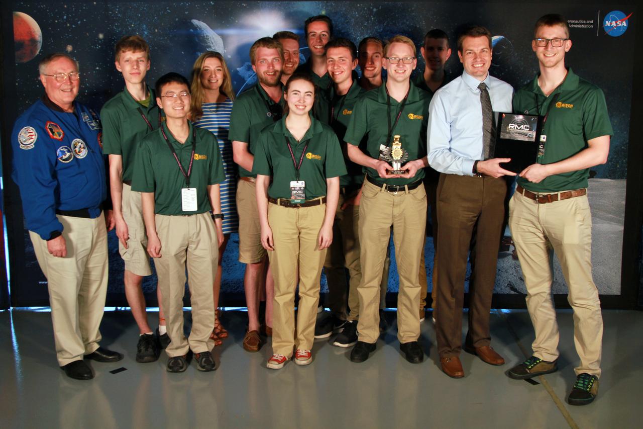 NASA's 9th Annual Robotic Mining Competition concludes with an awards ceremony May 18, 2018, at the Apollo/Saturn V Center at the Kennedy Space Center Visitor Complex in Florida. The team from North Dakota University in collaboration with James Madison University received first place in the Slide Presentation and Demonstration award category. At left is retired NASA astronaut Jerry Ross. At right is Daniel Hull, lead presentation judge. More than 40 student teams from colleges and universities around the U.S. participated in the competition, May 14-18, by using their mining robots to dig in a supersized sandbox filled with BP-1, or simulated lunar soil, gravel and rocks, and participate in other competition requirements. The Robotic Mining Competition is a NASA Human Exploration and Operations Mission Directorate project designed to encourage students in science, technology, engineering and math, or STEM fields. The project provides a competitive environment to foster innovative ideas and solutions that could be used on NASA's deep space missions.