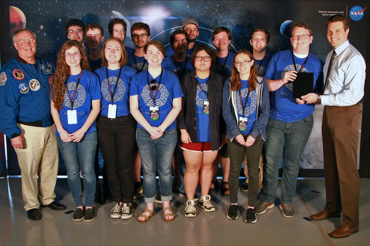 NASA's 9th Annual Robotic Mining Competition concludes with an awards ceremony May 18, 2018, at the Apollo/Saturn V Center at the Kennedy Space Center Visitor Complex in Florida. The team from Case Western Reserve University received third place in the Slide Presentation and Demonstration award category. At left is retired NASA astronaut Jerry Ross. At right is Daniel Hull, lead presentation judge. More than 40 student teams from colleges and universities around the U.S. participated in the competition, May 14-18, by using their mining robots to dig in a supersized sandbox filled with BP-1, or simulated lunar soil, gravel and rocks, and participate in other competition requirements. The Robotic Mining Competition is a NASA Human Exploration and Operations Mission Directorate project designed to encourage students in science, technology, engineering and math, or STEM fields. The project provides a competitive environment to foster innovative ideas and solutions that could be used on NASA's deep space missions.