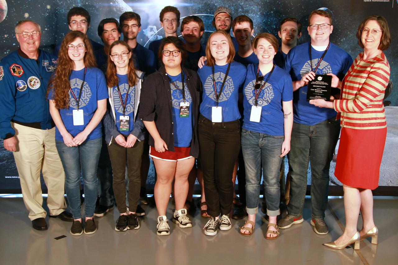NASA's 9th Annual Robotic Mining Competition concludes with an awards ceremony May 18, 2018, at the Apollo/Saturn V Center at the Kennedy Space Center Visitor Complex in Florida. The team from Case Western Reserve University received second place for their Systems Engineering Paper. At left is retired NASA astronaut Jerry Ross. At right is Jonette Stecklein, lead systems engineering paper judge. More than 40 student teams from colleges and universities around the U.S. participated in the competition, May 14-18, by using their mining robots to dig in a supersized sandbox filled with BP-1, or simulated lunar soil, gravel and rocks, and participate in other competition requirements. The Robotic Mining Competition is a NASA Human Exploration and Operations Mission Directorate project designed to encourage students in science, technology, engineering and math, or STEM fields. The project provides a competitive environment to foster innovative ideas and solutions that could be used on NASA's deep space missions.