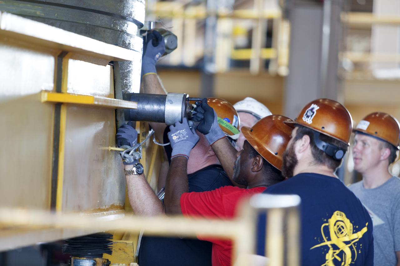 Jacobs technicians, on the Test and Operations Support Contract, check bolt fittings as they practice crane operations with an inert booster rocket segment in the Rotation, Processing and Surge Facility on June 22, 2018, at NASA's Kennedy Space Center in Florida. Dual cranes are being used to move the segment from vertical to horizontal, a maneuver known as a "breakover rotation." As part of routine processing operations for the agency's Space Launch System (SLS) rocket, the RPSF team will receive all of the solid rocket fuel segments for inspection and preparation prior to transporting them to the Vehicle Assembly Building for stacking on the mobile launcher. Many pathfinding operations are being done to prepare for launch of the SLS and Orion spacecraft on Exploration Mission-1 and deep space missions.