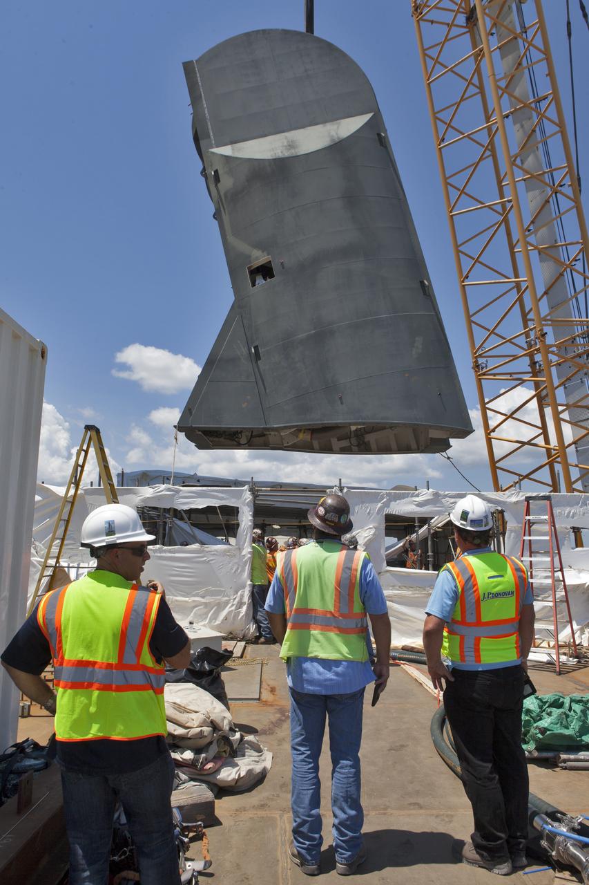 Construction workers with JP Donovan monitor operations as a crane is used to lower the first of two Tail Service Mast Umbilicals for installation on the 0-level deck of the mobile launcher on July 12, at NASA's Kennedy Space Center in Florida. The 35-foot-tall umbilical will connect to NASA's Space Launch System rocket core stage aft section and provide liquid oxygen and electrical cable connections to the core stage engine section to support propellant handling during prelaunch operations. The installation brings Exploration Ground Systems one step closer to supporting prelaunch operations for the agency's SLS rocket and Orion spacecraft on Exploration Mission-1 and deep space destinations.