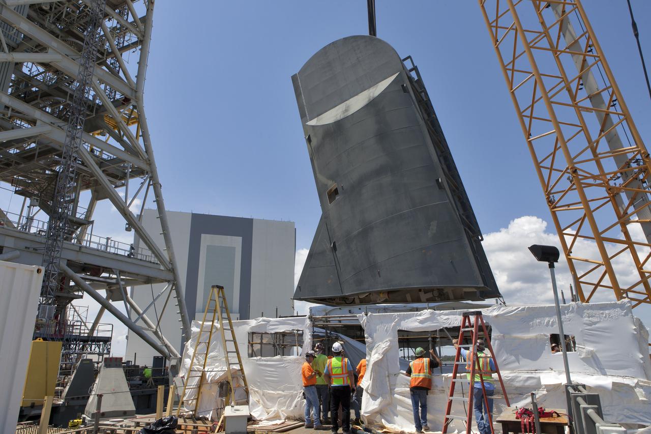 Construction workers with JP Donovan monitor operations as a crane is used to lower the first of two Tail Service Mast Umbilicals for installation on the 0-level deck of the mobile launcher on July 12, at NASA's Kennedy Space Center in Florida. The 35-foot-tall umbilical will connect to NASA's Space Launch System rocket core stage aft section and provide liquid oxygen and electrical cable connections to the core stage engine section to support propellant handling during prelaunch operations. The installation brings Exploration Ground Systems one step closer to supporting prelaunch operations for the agency's SLS rocket and Orion spacecraft on Exploration Mission-1 and deep space destinations.