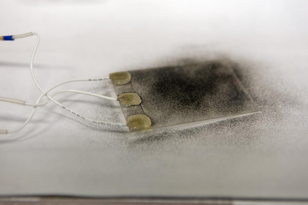 In the Electrostatics and Surface Physics Laboratory at NASA's Kennedy Space Center in Florida on Thursday, July 19, 2018, an Electrostatic Dust Shield has been covered with dust similar to that which may be encountered by astronauts exploring the Moon or Mars. Scientists are developing the dust shield to help mitigate the problem of dust on equipment, astronauts' space suits and helmet visors. The device is slated for analysis aboard International Space Station in the spring of 2019 to verify the effects of the space environment.