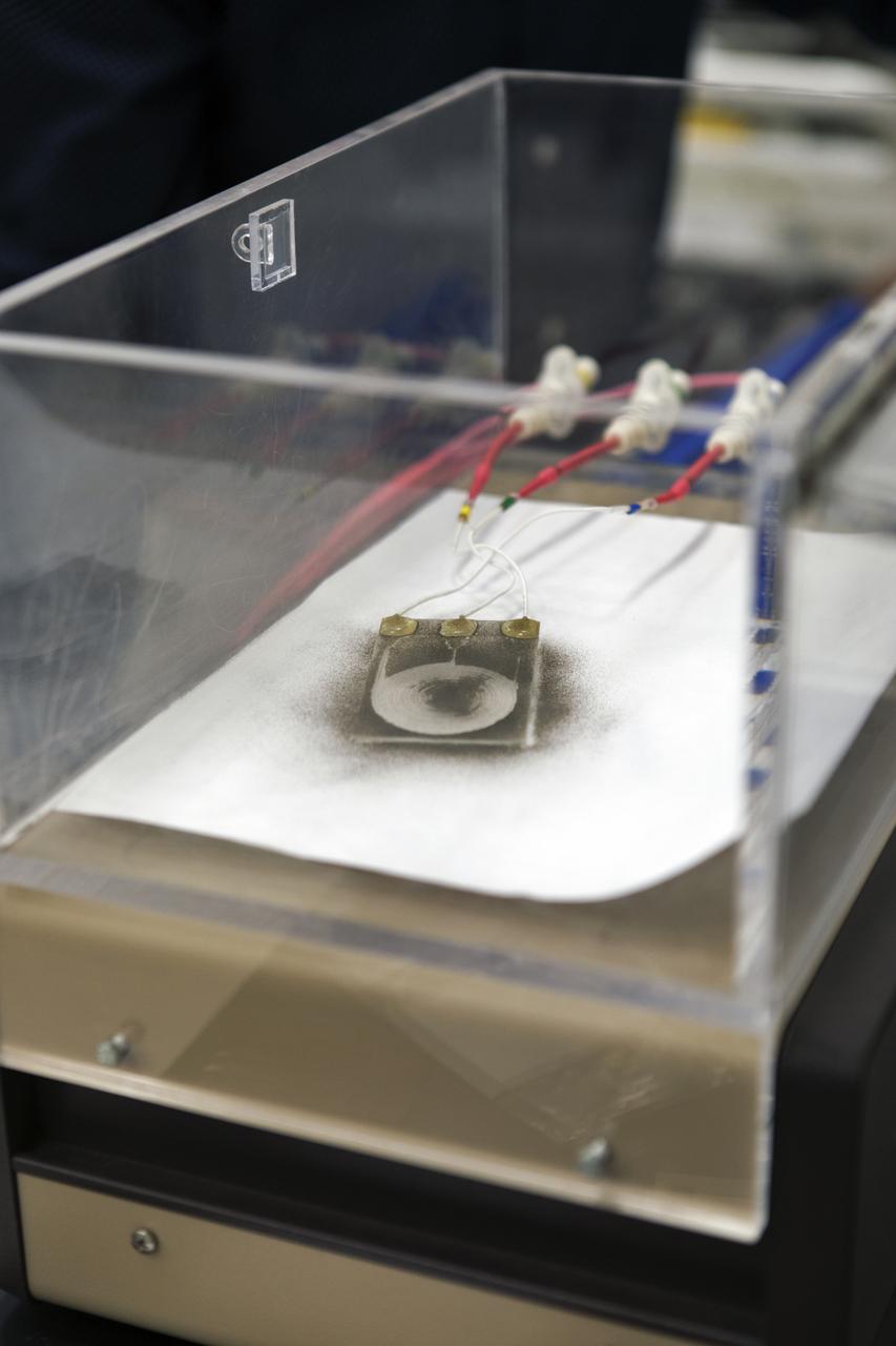 In the Electrostatics and Surface Physics Laboratory at NASA's Kennedy Space Center in Florida on Thursday, July 19, 2018, an experiment is underway in which an Electrostatic Dust Shield has been covered with dust similar to that which may be encountered by astronauts exploring the Moon or Mars. When activated, the device shakes off the dust. Scientists are developing the dust shield to help mitigate the problem of dust on equipment, astronauts' space suits and helmet visors. The device is slated for analysis aboard International Space Station in the spring of 2019 to verify the effects of the space environment.