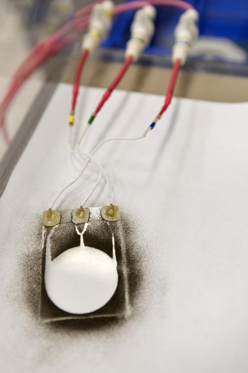 In the Electrostatics and Surface Physics Laboratory at NASA's Kennedy Space Center in Florida on Thursday, July 19, 2018, an experiment is underway in which an Electrostatic Dust Shield was been covered with dust similar to that which may be encountered by astronauts exploring the Moon or Mars. When activated, the device shook off the dust. Scientists are developing the dust shield to help mitigate the problem of dust on equipment, astronauts' space suits and helmet visors. The device is slated for analysis aboard International Space Station in the spring of 2019 to verify the effects of the space environment.