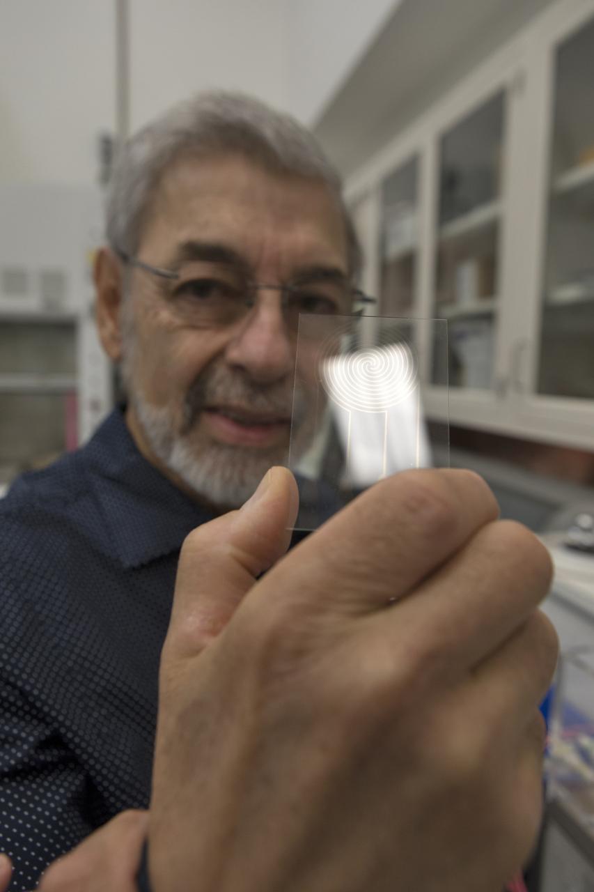 On Thursday, July 19, 2018, Dr. Carlos Calle, lead scientist in the Electrostatics and Surface Physics Laboratory at NASA's Kennedy Space Center in Florida, shows an Electrostatic Dust Shield that had been covered with dust similar to that which may be encountered by astronauts exploring the Moon or Mars. When activated, the device shook off the dust. Scientists are developing the dust shield to help mitigate the problem of dust on equipment, astronauts' space suits and helmet visors. The device is slated for analysis aboard International Space Station in the spring of 2019 to verify the effects of the space environment.