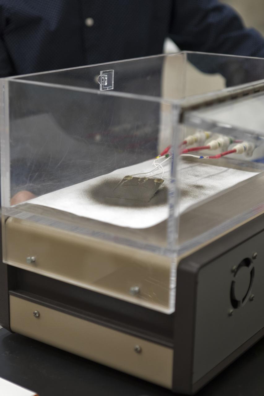 In the Electrostatics and Surface Physics Laboratory at NASA's Kennedy Space Center in Florida on Thursday, July 19, 2018, an experiment is underway in which an Electrostatic Dust Shield was been covered with dust similar to that which may be encountered by astronauts exploring the Moon or Mars. When activated, the device shook off the dust. Scientists are developing the dust shield to help mitigate the problem of dust on equipment, astronauts' space suits and helmet visors. The device is slated for analysis aboard International Space Station in the spring of 2019 to verify the effects of the space environment.