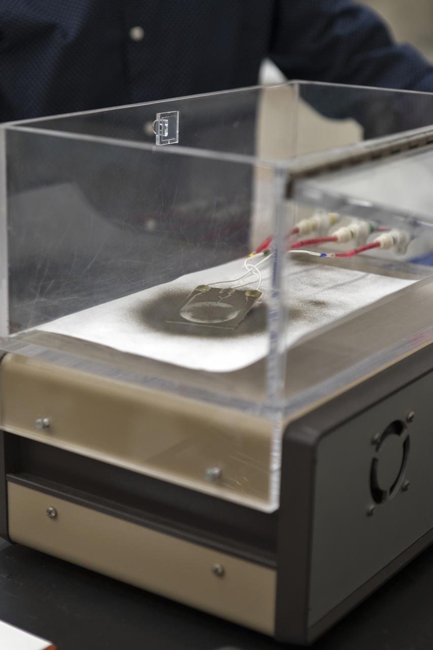 In the Electrostatics and Surface Physics Laboratory at NASA's Kennedy Space Center in Florida on Thursday, July 19, 2018, an experiment is underway in which an Electrostatic Dust Shield was been covered with dust similar to that which may be encountered by astronauts exploring the Moon or Mars. When activated, the device shook off the dust. Scientists are developing the dust shield to help mitigate the problem of dust on equipment, astronauts' space suits and helmet visors. The device is slated for analysis aboard International Space Station in the spring of 2019 to verify the effects of the space environment.