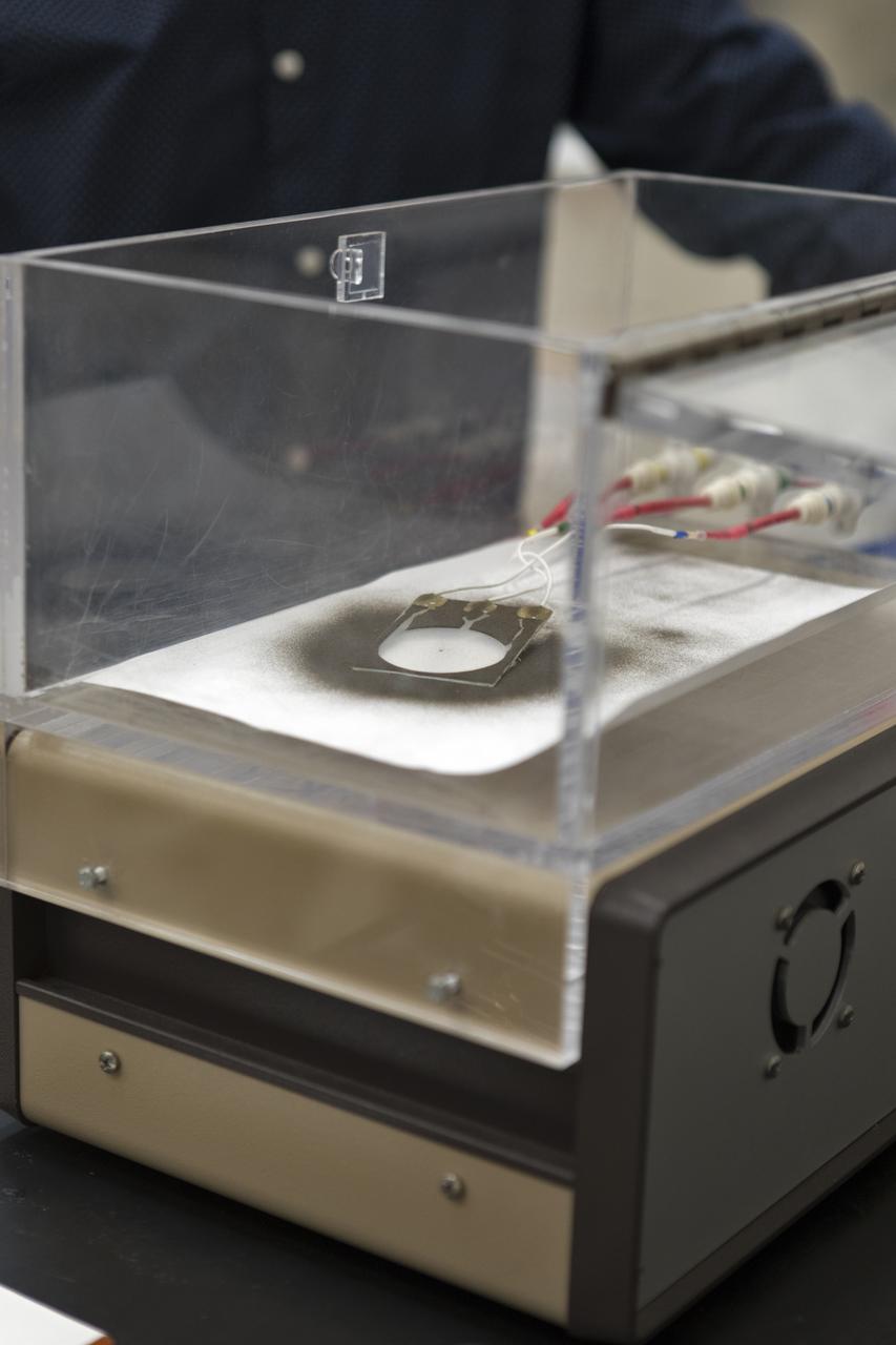 In the Electrostatics and Surface Physics Laboratory at NASA's Kennedy Space Center in Florida on Thursday, July 19, 2018, an experiment is underway in which an Electrostatic Dust Shield was been covered with dust similar to that which may be encountered by astronauts exploring the Moon or Mars. After activation, the device shook off the dust. Scientists are developing the dust shield to help mitigate the problem of dust on equipment, astronauts' space suits and helmet visors. The device is slated for analysis aboard International Space Station in the spring of 2019 to verify the effects of the space environment.