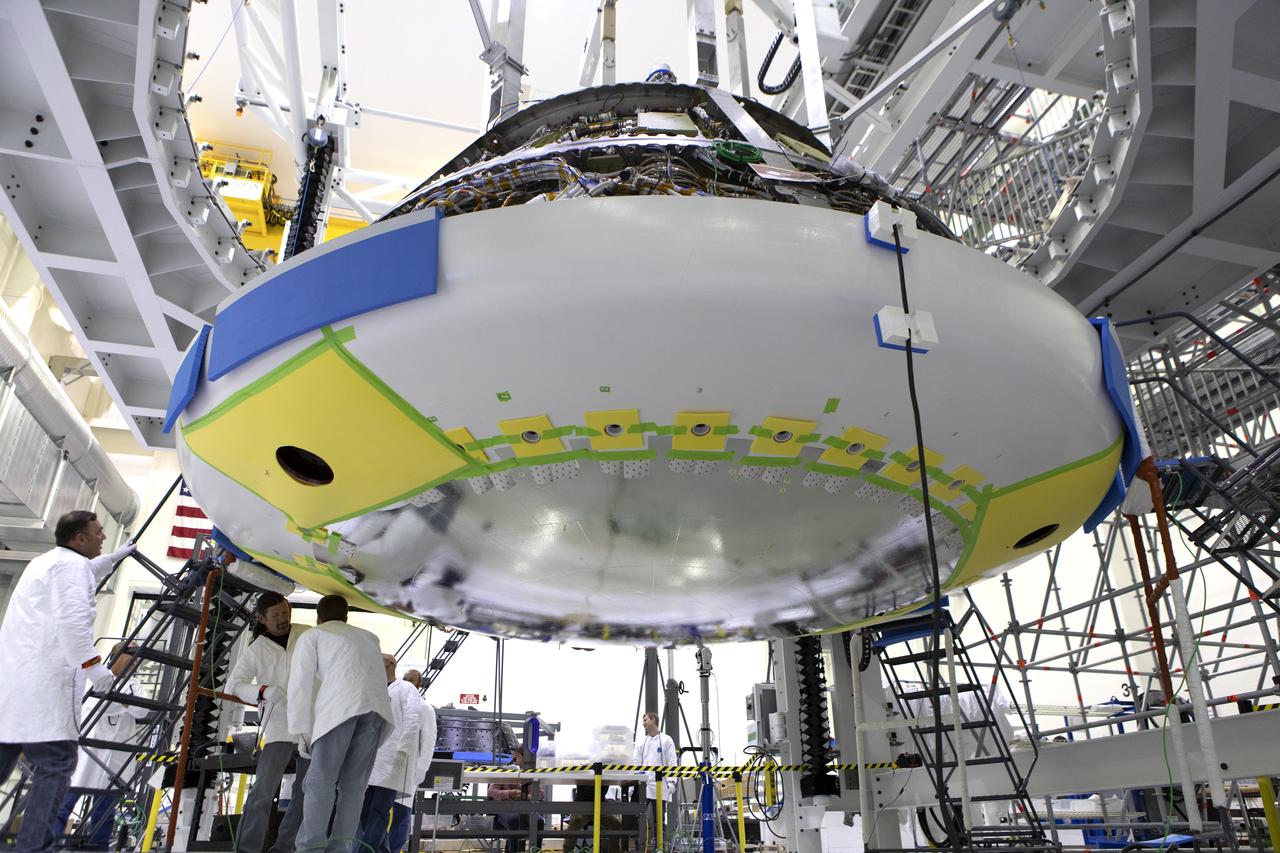 Lockheed Martin engineers and technicians are installing the heat shield to the Orion crew module July 25, 2018, inside the Neil Armstrong Operations and Checkout Building high bay at NASA's Kennedy Space Center in Florida. Orion is being prepared for Exploration Mission-1 (EM-1), the first unscrewed integrated flight test atop NASA's Space Launch System rocket. The heat shield will need to withstand temperatures of up to 5,000 degrees Fahrenheit during Orion's descent and re-entry through the Earth's atmosphere before it splashes down in the Pacific Ocean.