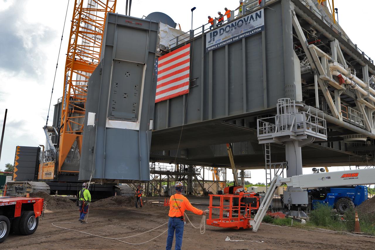 Construction workers with JP Donovan assist as a crane lifts the second of two Tail Service Mast Umbilicals up for installation on the 0-level deck of the mobile launcher on July 27, at NASA's Kennedy Space Center in Florida. The 35-foot-tall umbilical will connect to NASA's Space Launch System rocket core stage aft section and provide liquid hydrogen and electrical cable connections to the core stage engine section to support propellant handling during prelaunch operations. The installation brings Exploration Ground Systems one step closer to supporting prelaunch operations for the agency's SLS rocket and Orion spacecraft on Exploration Mission-1 and deep space destinations.