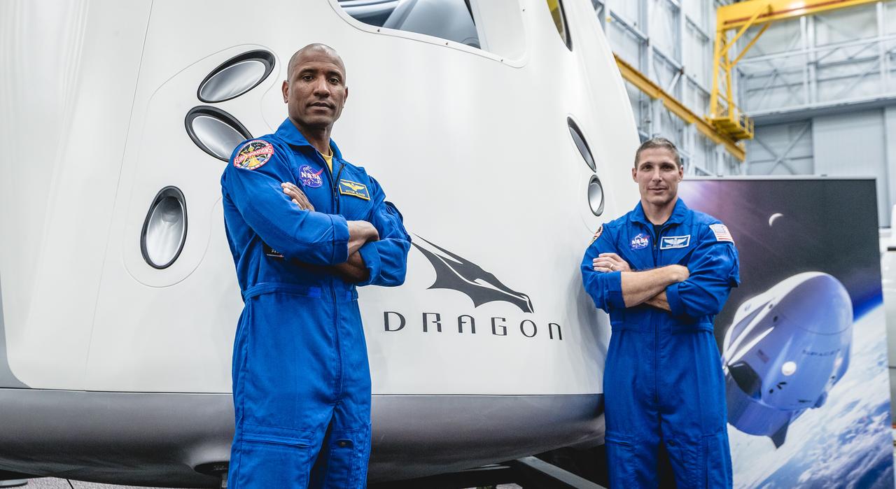 NASA astronauts, from left, Victor Glover and Mike Hopkins, assigned to fly on the first operational mission of SpaceX's Crew Dragon, are in front of the spacecraft at NASA's Johnson Space Center in Houston on Aug. 2, 2018, ahead of the agency's announcement of their commercial crew assignment Aug. 3. Nine U.S. astronauts were selected for commercial crew flight assignments on the first test flights and operational missions for SpaceX's Crew Dragon and Boeing's CST-100 Starliner.