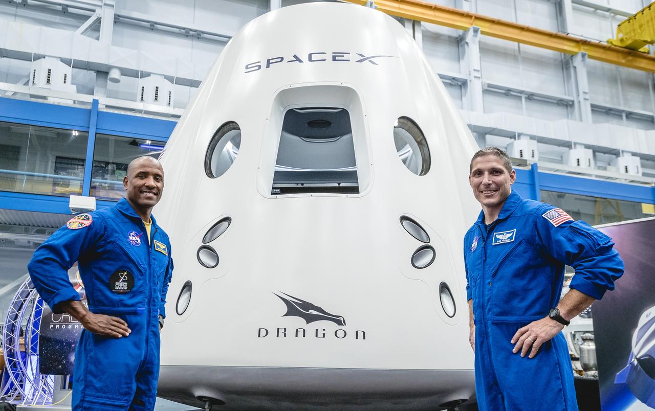 NASA astronauts, from left, Victor Glover and Mike Hopkins, assigned to fly on the first operational mission of SpaceX's Crew Dragon, pose in front of the spacecraft at NASA's Johnson Space Center in Houston on Aug. 2, 2018, ahead of the agency's announcement of their commercial crew assignment Aug. 3. Nine U.S. astronauts were selected for commercial crew flight assignments on the first test flights and operational missions for SpaceX's Crew Dragon and Boeing's CST-100 Starliner.