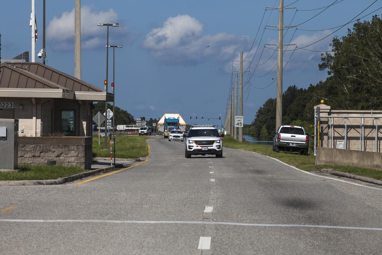 A super-wide truck carrying the Orion crew module pressure vessel for Exploration Mission-2 approaches the entrance gate at NASA's Kennedy Space Center in Florida on Aug. 24, 2018. The pressure vessel was transported in its Crew Module Transportation Fixture by truck from Michoud Assembly Facility near New Orleans. The pressure vessel is Orion's primary structure that holds the pressurized atmosphere astronauts will breathe and work in while in the vacuum of deep space. It will be moved into the Neil Armstrong Operations and Checkout Building high bay, where it will be secured on a precision alignment tool to begin preparing it for flight.