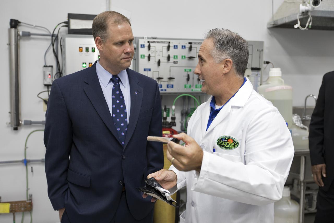NASA Administrator Jim Bridenstine, at left, tours the Space Station Processing Facility at NASA's Kennedy Space Center in Florida, on Aug. 7, 2018. At right, Trent Smith, Veggie project manager, displays a seed packet and plant pillow for the Veggie plant growth system. Bridenstine also received updates on research and technology accomplishments.