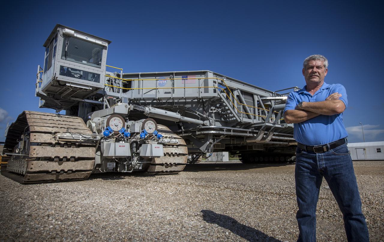 Sam Dove, a crawler-transporter engineer with Jacobs on the Test and Operations Support Contract, stands in front of crawler-transporter 2 on the crawlerway at NASA's Kennedy Space Center in Florida, on Aug. 27, 2018. CT-2 will carry the mobile launcher for the first time to Launch Pad 39B for a fit check of key systems that will support the launch of the agency's Space Launch System rocket and Orion spacecraft on Exploration Mission-1. The crawler also will carry the mobile launcher to the Vehicle Assembly Building for system checks and fit checks with the 10 levels of new platforms in High Bay 3.