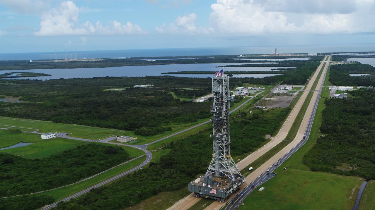 An aerial view of NASA's mobile launcher (ML) atop crawler-transporter 2 as it moves along the crawlerway to Launch Pad 39B on Aug. 30, 2018, at the agency's Kennedy Space Center in Florida. The ML will undergo a fit check on the surface of the pad, followed by several days of systems testing. The 380-foot-tall mobile launcher is equipped with the crew access arm and several umbilicals that will provide power, environmental control, pneumatics, communication and electrical connections to NASA's Space Launch System (SLS) and Orion spacecraft. Exploration Ground Systems is preparing the ground systems necessary to launch SLS and Orion on Exploration Mission-1, missions to the Moon and on to Mars.