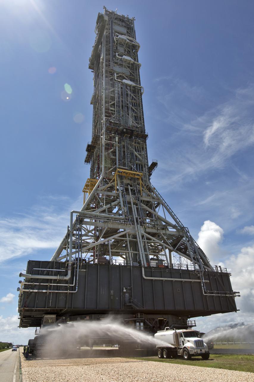 A truck sprays water to reduce the dust as NASA's crawler-transporter 2 (CT-2) with the mobile launcher (ML) atop slowly moves along the crawlerway on its trek to Launch Pad 39B on Aug. 31, 2018, at the agency's Kennedy Space Center in Florida. CT-2 will move the ML up to the surface of the pad where it will undergo a fit check, followed by several days of systems testing. The 380-foot-tall mobile launcher is equipped with the crew access arm and several umbilicals that will provide power, environmental control, pneumatics, communication and electrical connections to NASA's Space Launch System (SLS) and Orion spacecraft. Exploration Ground Systems is preparing the ground systems necessary to launch SLS and Orion on Exploration Mission-1, missions to the Moon and on to Mars.