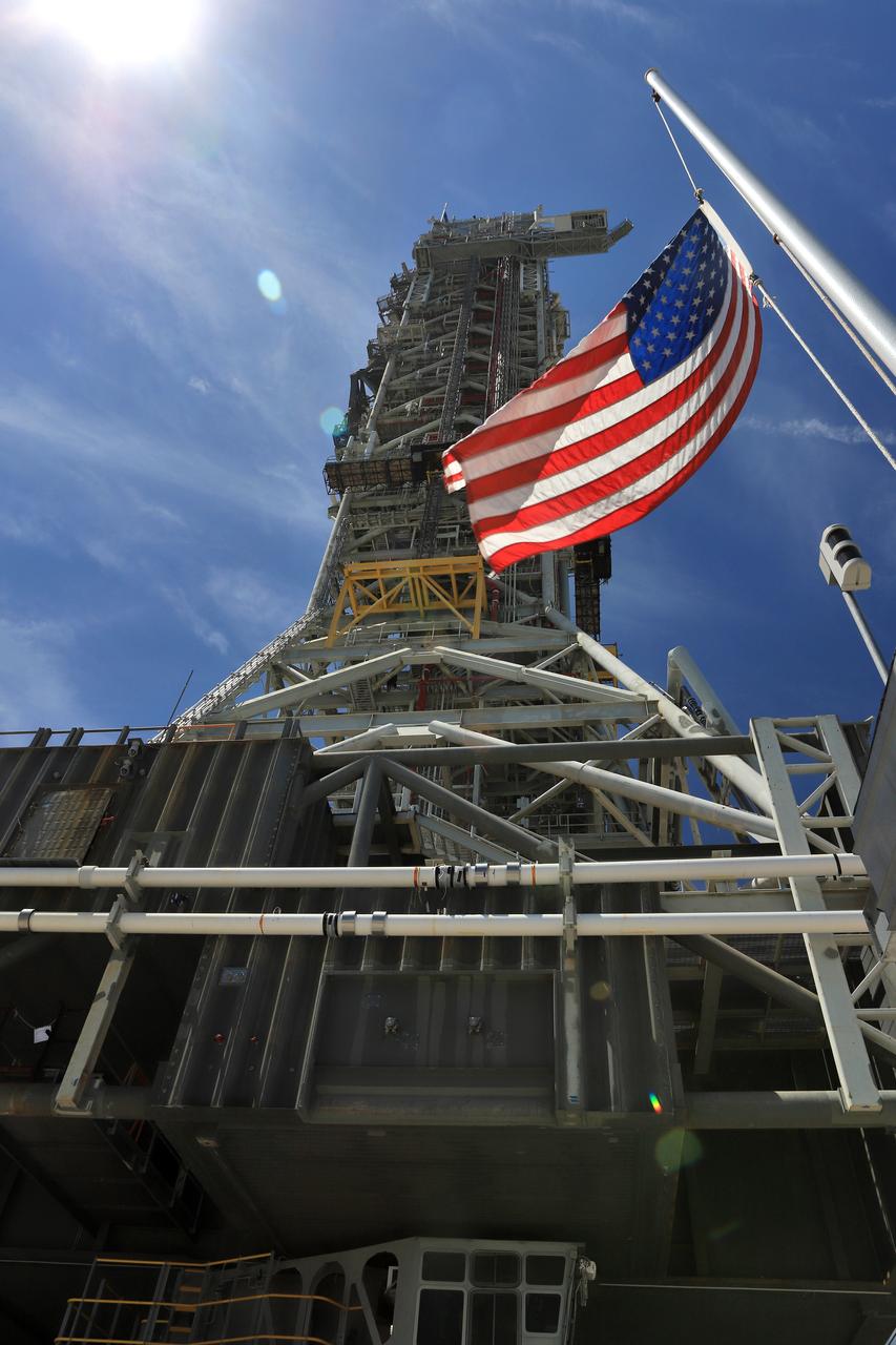 The American flag is in view as NASA's crawler-transporter 2 (CT-2) with the mobile launcher (ML) atop slowly moves along the crawlerway on its trek to Launch Pad 39B on Aug. 31, 2018, at the agency's Kennedy Space Center in Florida. CT-2 will move the ML up to the surface of the pad where it will undergo a fit check, followed by several days of systems testing. The 380-foot-tall mobile launcher is equipped with the crew access arm and several umbilicals that will provide power, environmental control, pneumatics, communication and electrical connections to NASA's Space Launch System (SLS) and Orion spacecraft. Exploration Ground Systems is preparing the ground systems necessary to launch SLS and Orion on Exploration Mission-1, missions to the Moon and on to Mars.