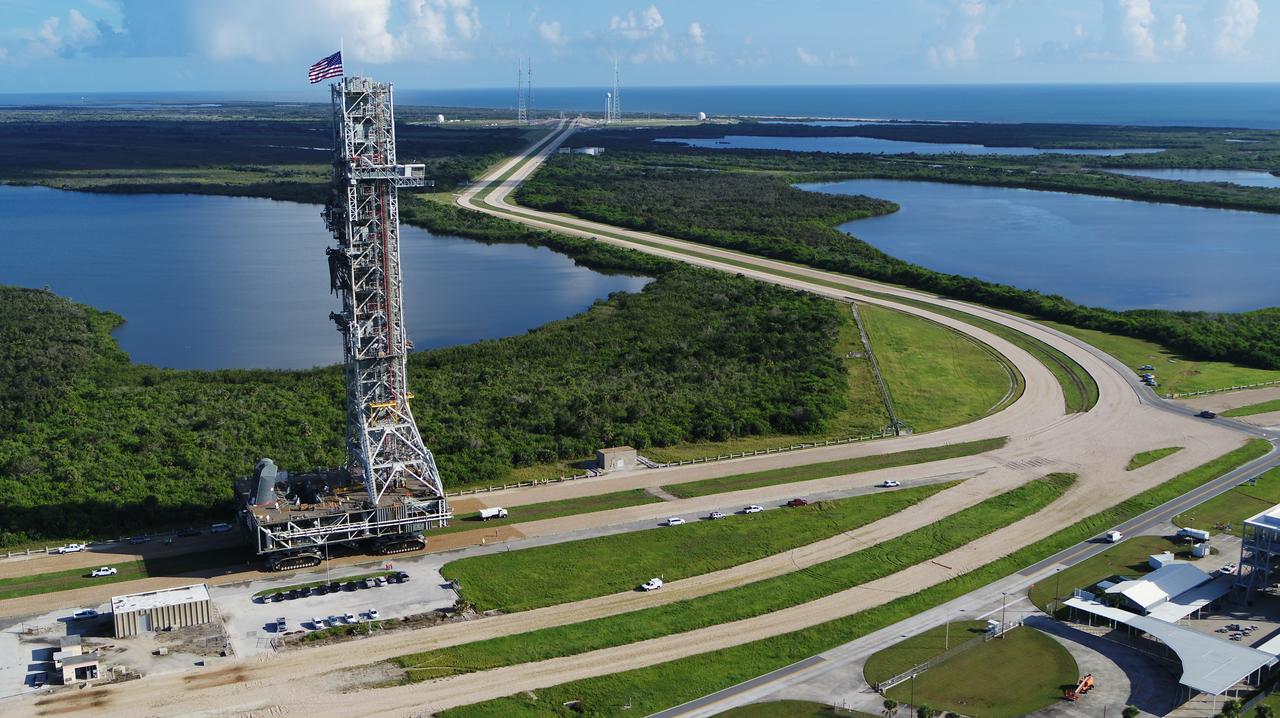 An aerial view of NASA's mobile launcher (ML) atop crawler-transporter 2 as it moves along the crawlerway to Launch Pad 39B on Aug. 31, 2018, at the agency's Kennedy Space Center in Florida. The ML will undergo a fit check on the surface of the pad, followed by several days of systems testing. The 380-foot-tall mobile launcher is equipped with the crew access arm and several umbilicals that will provide power, environmental control, pneumatics, communication and electrical connections to NASA's Space Launch System (SLS) and Orion spacecraft. Exploration Ground Systems is preparing the ground systems necessary to launch SLS and Orion on Exploration Mission-1, missions to the Moon and on to Mars.