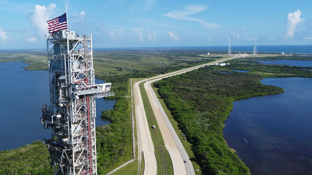 An aerial view of NASA's mobile launcher (ML) atop crawler-transporter 2 as it moves along the crawlerway to Launch Pad 39B on Aug. 31, 2018, at the agency's Kennedy Space Center in Florida. In view on top of the ML is the American flag. The ML will undergo a fit check on the surface of the pad, followed by several days of systems testing. The 380-foot-tall mobile launcher is equipped with the crew access arm and several umbilicals that will provide power, environmental control, pneumatics, communication and electrical connections to NASA's Space Launch System (SLS) and Orion spacecraft. Exploration Ground Systems is preparing the ground systems necessary to launch SLS and Orion on Exploration Mission-1, missions to the Moon and on to Mars.