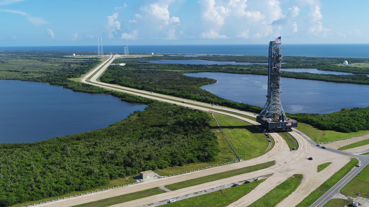 An aerial view of NASA's mobile launcher (ML) atop crawler-transporter 2 as it moves along the crawlerway, making the turn to Launch Pad 39B on Aug. 31, 2018, at the agency's Kennedy Space Center in Florida. In view on top of the ML is the American flag. The ML will undergo a fit check on the surface of the pad, followed by several days of systems testing. The 380-foot-tall mobile launcher is equipped with the crew access arm and several umbilicals that will provide power, environmental control, pneumatics, communication and electrical connections to NASA's Space Launch System (SLS) and Orion spacecraft. Exploration Ground Systems is preparing the ground systems necessary to launch SLS and Orion on Exploration Mission-1, missions to the Moon and on to Mars.