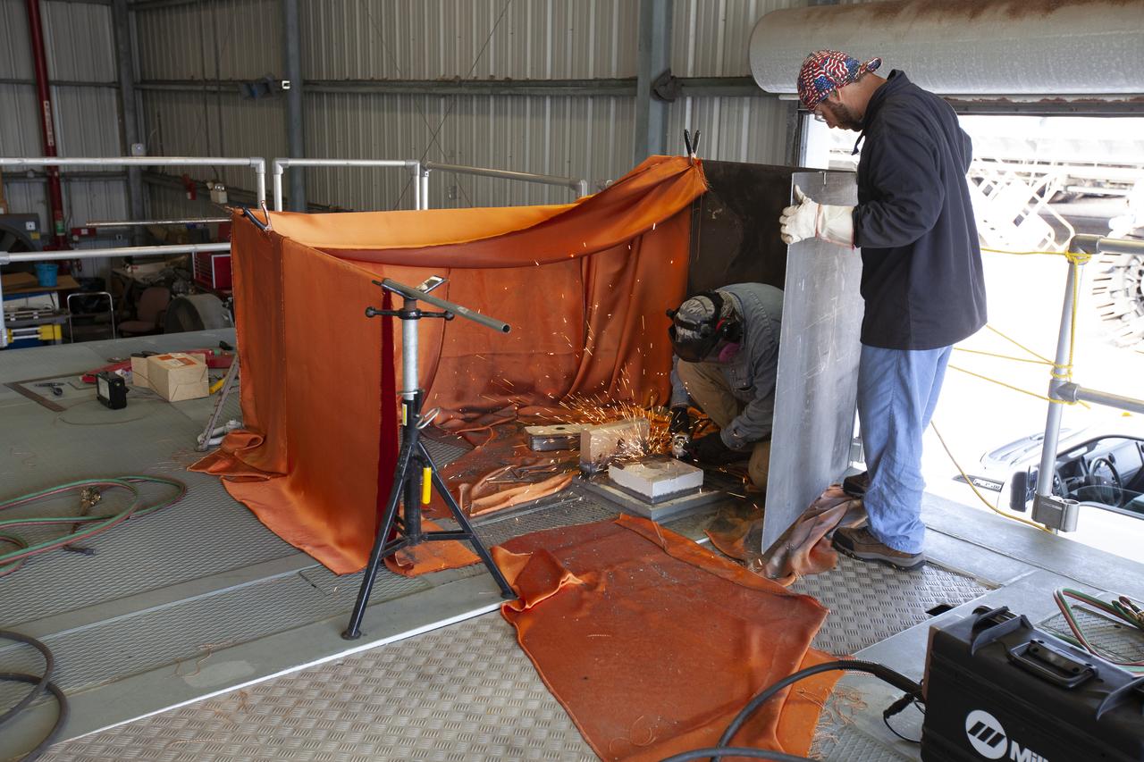 Jacobs technicians from the Launch Equipment Shop perform welding on the KAMAG spacecraft transporter on Oct. 26, 2018, inside a facility at the crawler yard at NASA’s Kennedy Space Center in Florida. The transporter is designed to carry heavy loads. Welding is being performed on the attach points that will hold the Orion transportation pallet in place. Testing of the pallet will be performed to support validation and verification of the attach fittings in the Multi-Payload Processing Facility.